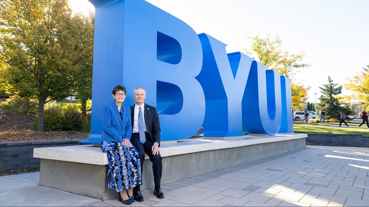 Elder and Sister Bednar seated in front of a large BYU-Idaho campus sign
