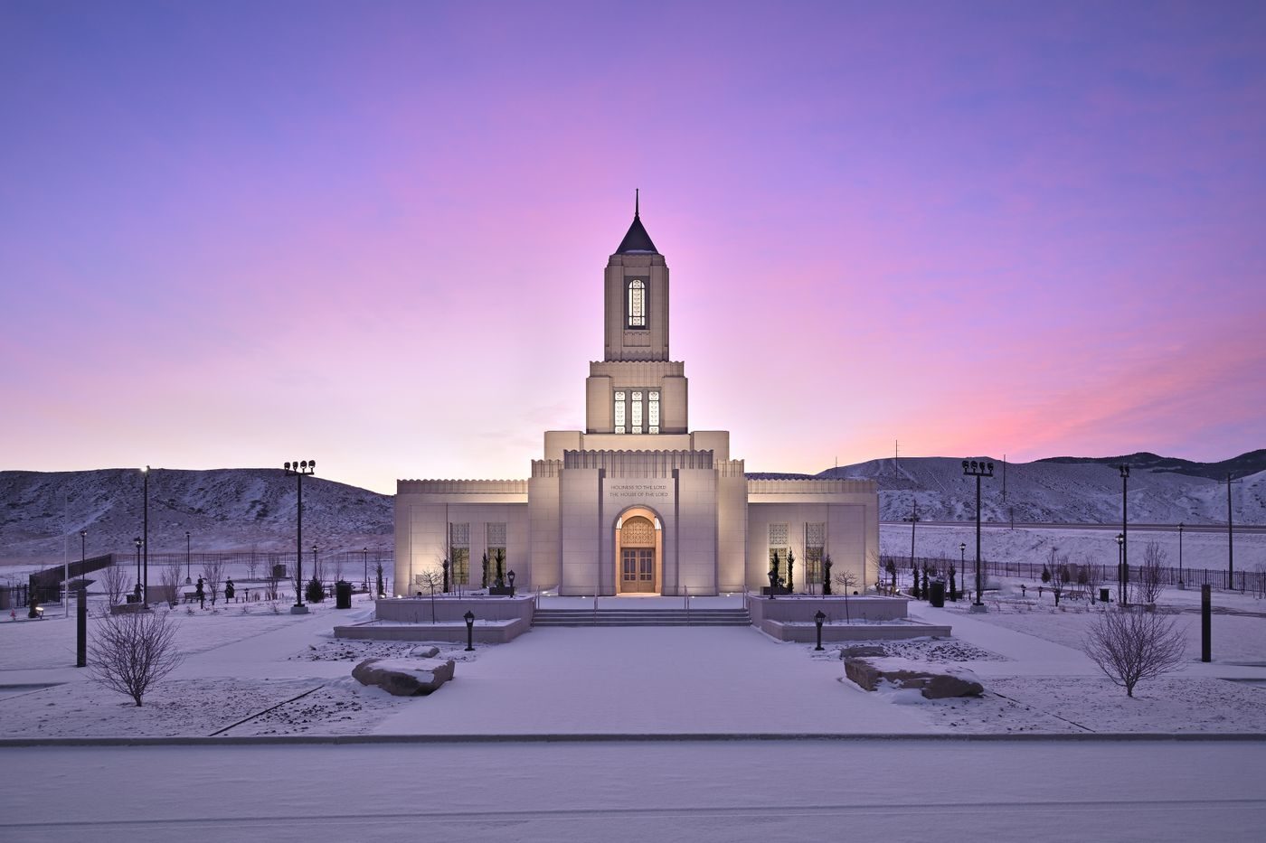 The Casper Wyoming Temple in winter with snow on the grounds and hills under a pink sky