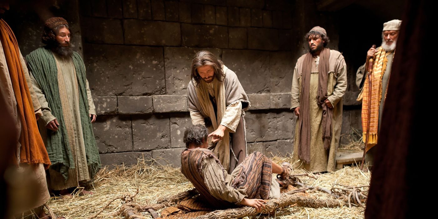 Artwork of Jesus Christ kneeling to minister to a man lying on the ground as others look on