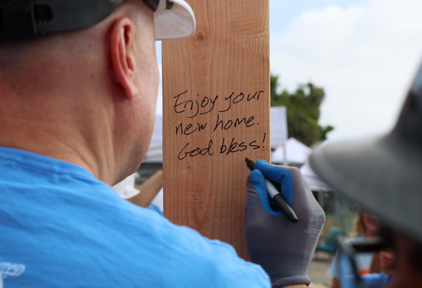 A volunteer writing "Enjoy your new home. God bless!" on a wooden stud at the Habitat for Humanity build