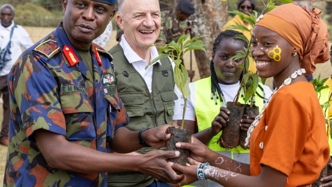 Elder Paul B. Pieper and Kenyan leaders handing a tree seedling to a student at a planting event in Thogoto, Kenya