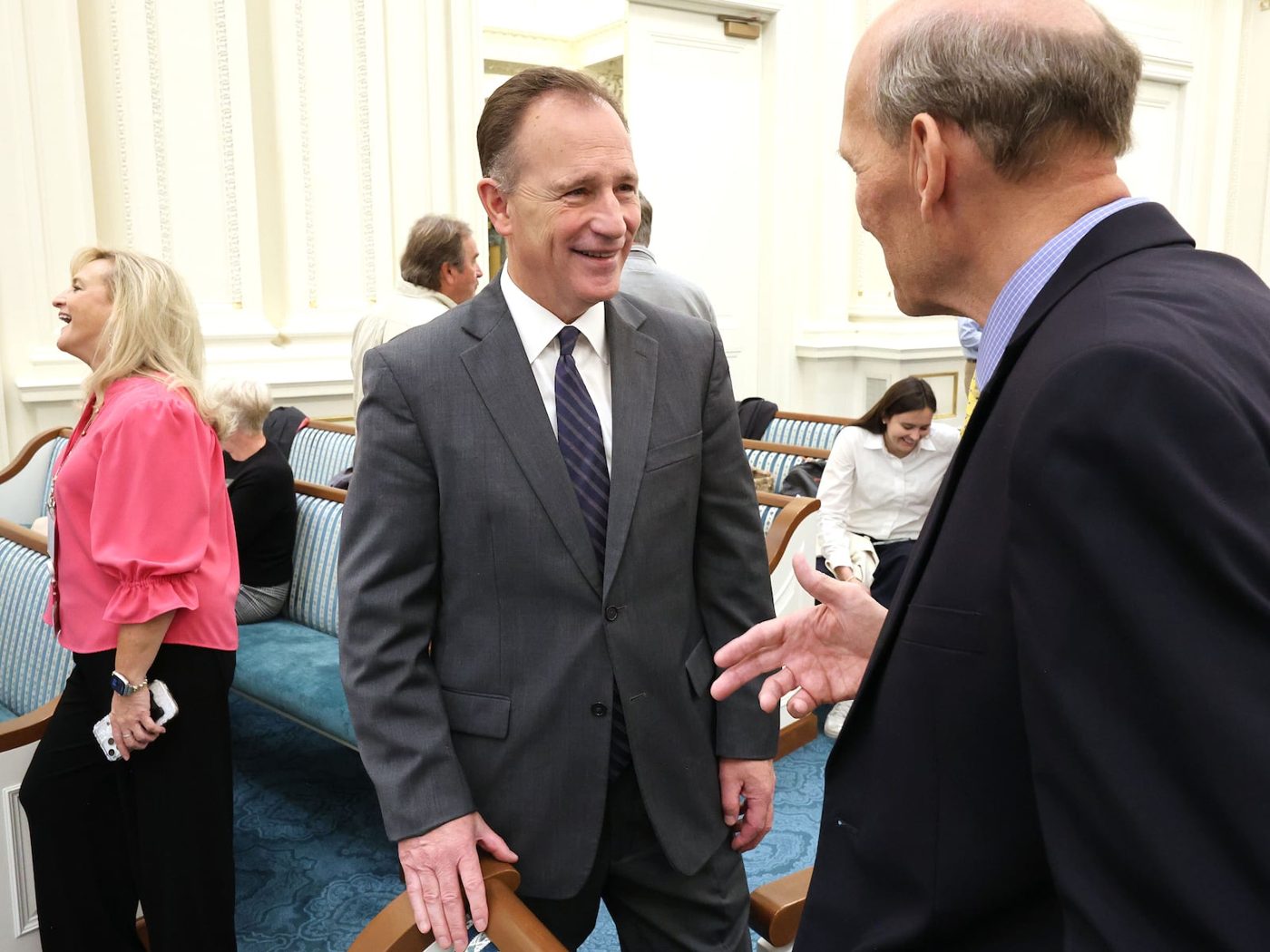 Elder Kyle S. McKay smiling as he greets an attendee in the Joseph Smith Memorial Building chapel before the Church History Symposium