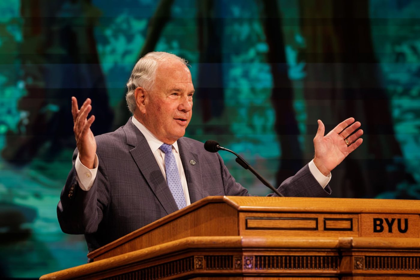 Elder Ronald A. Rasband gesturing at the BYU pulpit in the Marriott Center