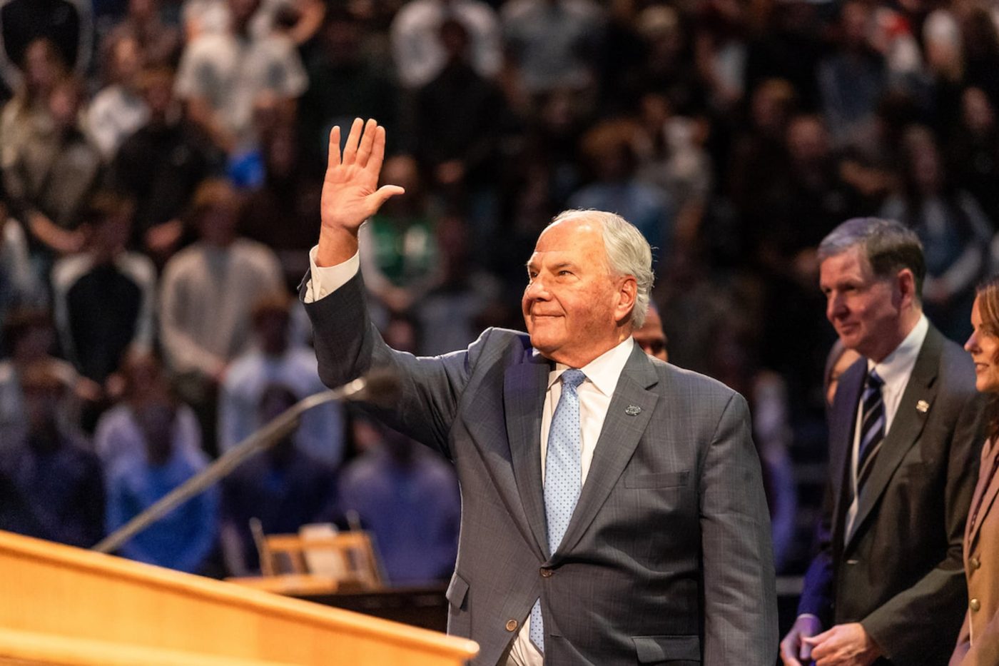 Elder Ronald A. Rasband raising his hand to wave to the crowd in the Marriott Center