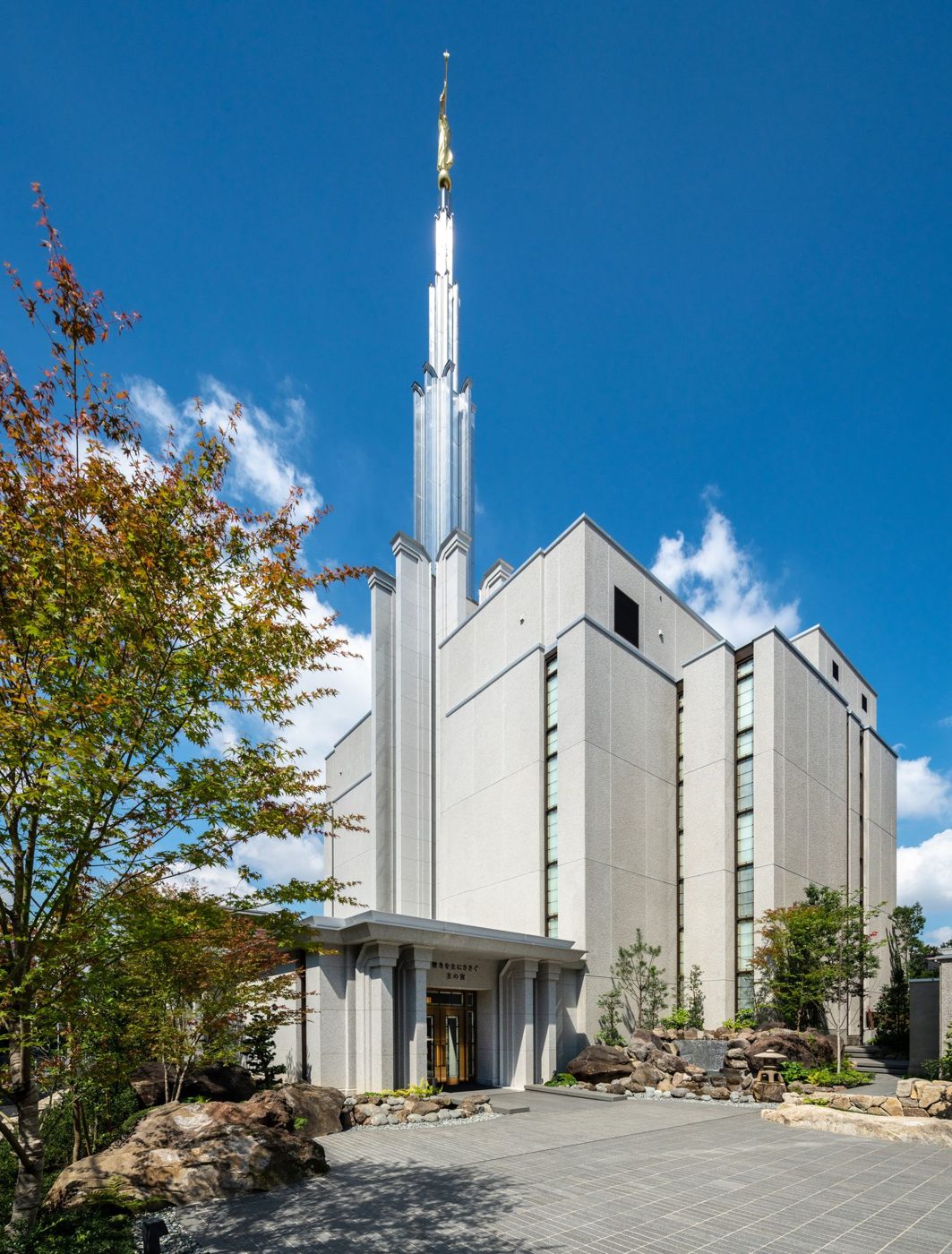 The white Tokyo Japan Temple with its single tall spire under a blue sky