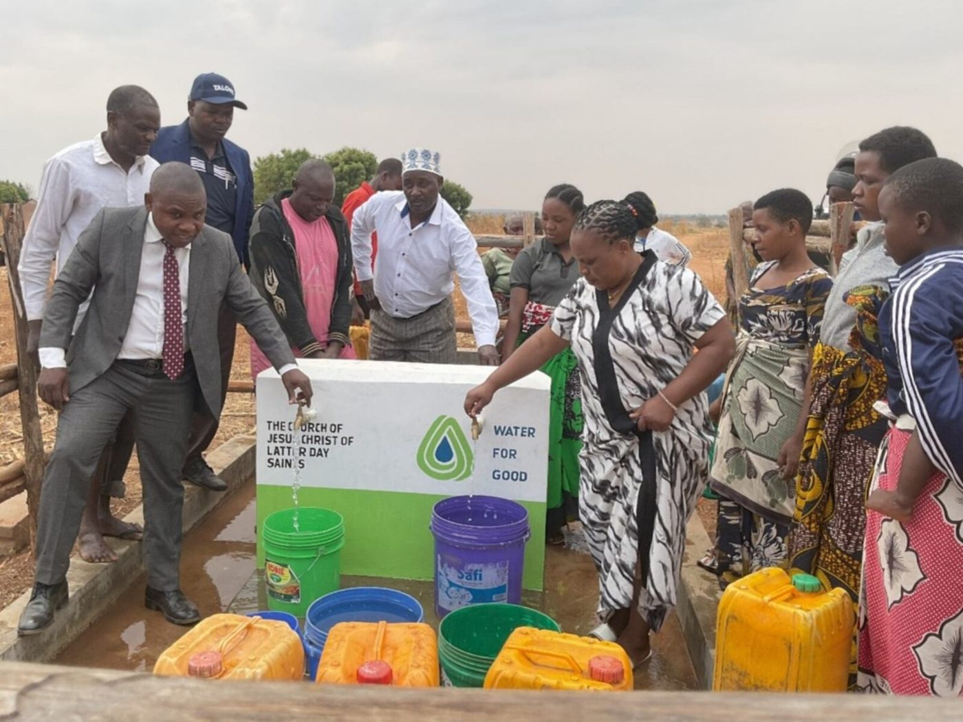 A district president opening a new water tap as villagers in Tanzania fill colorful containers